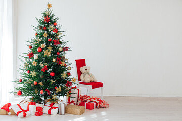 Big beautiful christmas tree decorated with beautiful shiny baubles and many different presents on wooden floor.