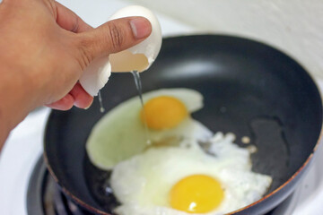 Cracking egg shell over frying pan to make egg