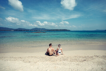 Sensual young couple in swimsuits laying on the sand by the sea over sky and tropical island background. Phuket. Thailand.