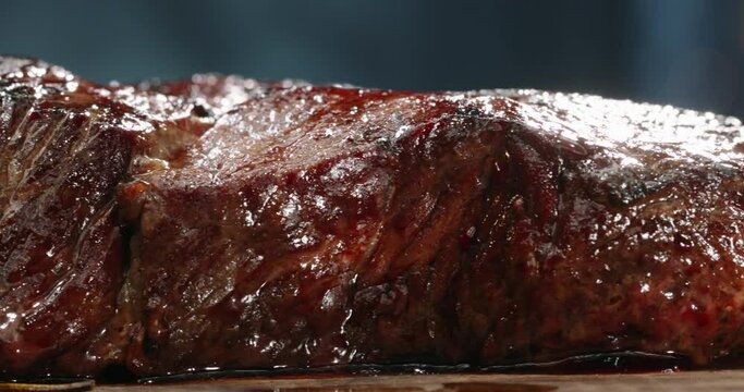 Close up shot of a juicy freshly grilled steak. Big piece of tasty meat straight from the grid. Smoke rising from delicious meal on chef's preparation table 4k footage