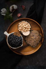 Overhead view of some raw dried nutritive brown legumes on a wooden tray over a dark cloth.