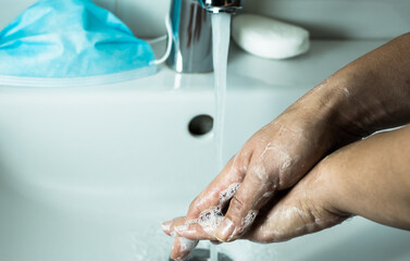 Washing hands with soap for corona virus prevention, hygiene to stop spreading Covid-19. Mask in the background