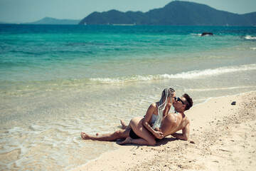 Sensual young couple in swimsuits laying on the sand by the sea over sky and tropical island background. Phuket. Thailand.