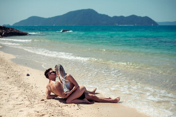 Fototapeta na wymiar Sensual young couple in swimsuits laying on the sand by the sea over sky and tropical island background. Phuket. Thailand.