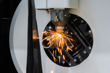 Laser cutting machine working with cylindrical metal workpiece with sparks at factory, plant. Metalworking, industrial, equipment, technology, machining, manufacturing concept