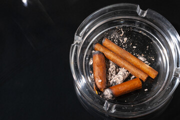 Ash tray full of cigarette butts on black background