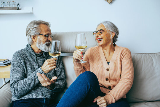 Senior couple at home celebrating and cheering with wine glasses