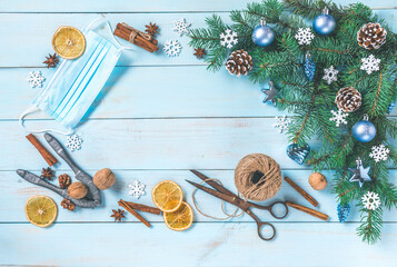 Christmas blue background, spices, dried fruits, face mask. Covid-19, coronavirus awareness. Festive decoration, corner pine tree branches, blue silver baubles, snowflakes. Top view, copy space.