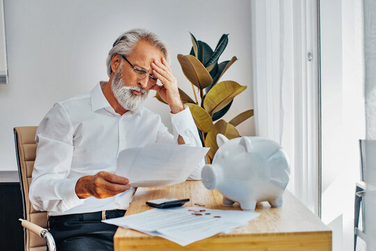 Portrait Of A Senior White Hair Man At Home Desk Worried About Money, Contracts And Paying Bills Or Loans