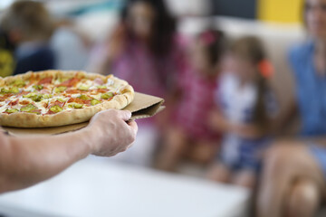 Man delivering cooked homemade hot pizza close-up to family. In background, family wait for italian food.