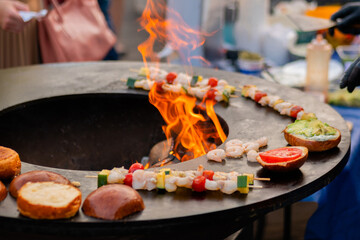 Process of preparing shrimp, prawn skewers and burgers with avocado and tomato on brazier with hot flame at local food market - close up. Outdoor cooking, seafood, gastronomy, street food concept