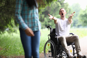 Obraz premium Disabled man sit in wheelchair in park, stretches his arms forward and shouts no. Woman break off relations with disabled man and leave.