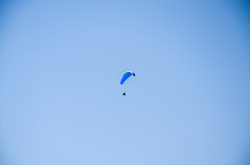 Paraglider flying over the mountains against the blue sky in clear weather. Extreme sport, lifestyle and freedom concept