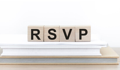 Wooden cubes labeled RSVP that lies on a stack of books on isolated light background.