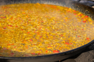 Process of cooking yellow paella with tomato, rice, spice, saffron in huge paella pan at summer outdoor food market: close up. Spanish cuisine, seafood, gastronomy, street food concept