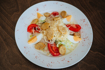 Salad with croutons, tomatoes and eggs, sprinkled with cheese and cabbage. Snack on a white round plate