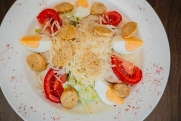 Salad with croutons, tomatoes and eggs, sprinkled with cheese and cabbage. Snack on a white round plate