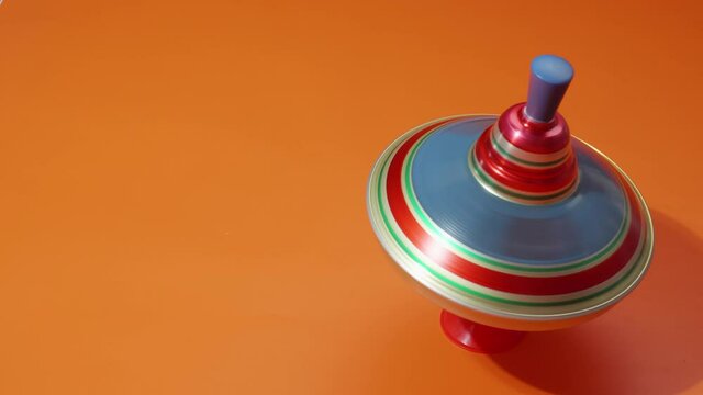Multicolored metal spinning top or whirligig top is traditional toy for preschool childs. Rotates in circle on orange surface.