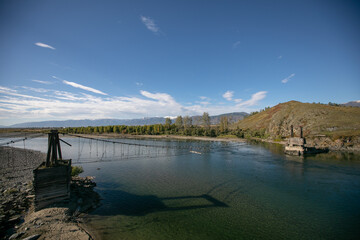 The very old hanging footbridge across river.Beautiful mountain landscape, blue river and coniferous forest