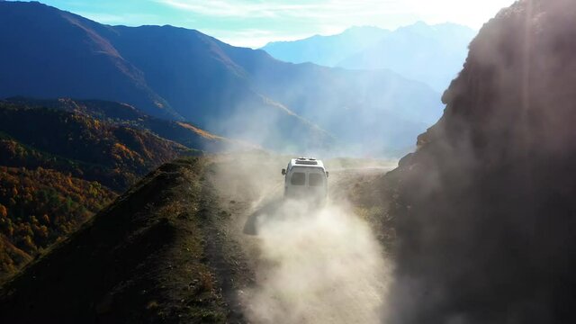 Drone camera follows car driving in mountains. Road dust cloud from under wheels