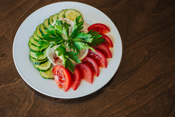 White round plate with chopped vegetables. Sliced tomatoes and cucumbers. Snack on the table.