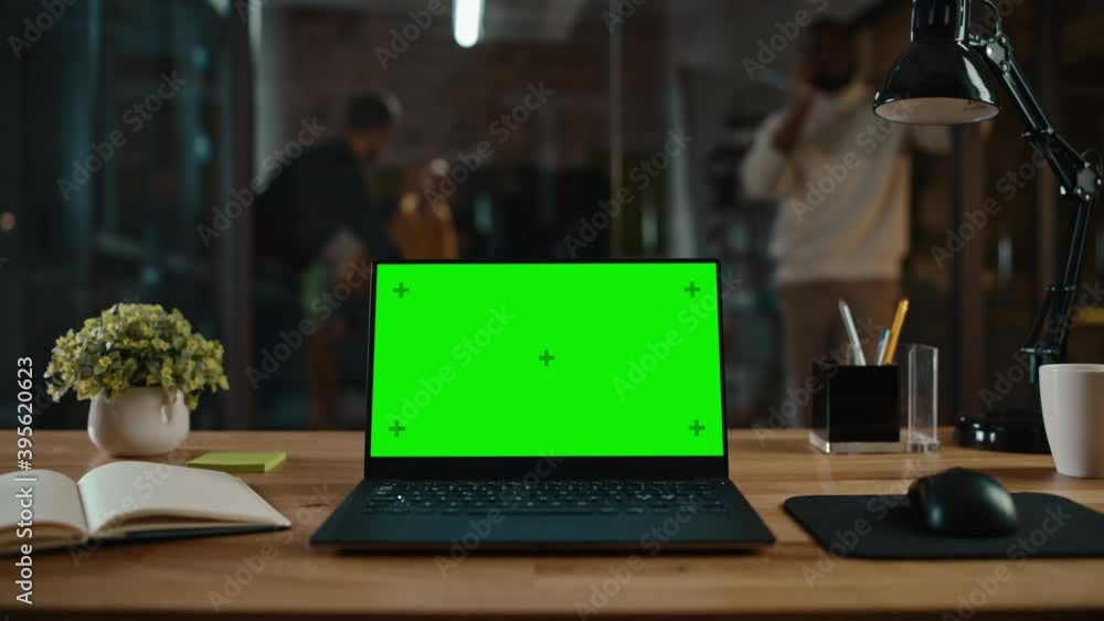 Poster Zoom In Footage of a Laptop Computer with Green Screen Mock Up Display on a Desk in a Busy Creative Office Environment. Isolated Template for Any Media Type. Authentic Hipster Agency Vibe. 