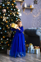 Happy little girl holding gift box by christmas tree Isolated.