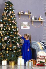 Merry Christmas and Happy Holidays. Cute little child girl is decorating the Christmas tree indoors.