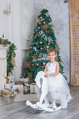 little girl riding a wooden horse near the fireplace and New Year tree