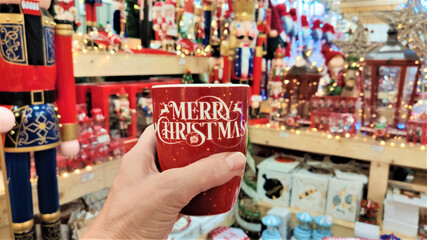female hand with red mug, merry christmas in shop with christmas decorations.