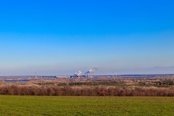 View of green wheat field and smoke pipes of factory at spring
