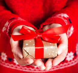 Young woman's hands in red pullover holding gift box with red ribbon. Close-up. Holiday gift....