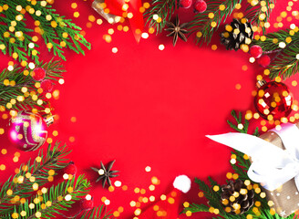 Frame made of fir branches, red berries, fir cones, gift boxes on red background. Christmas or New Year flatlay. Top view. Copy space.
