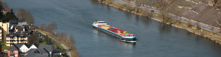 Inland cargo ship with colorful container freight passing vineyards and Bernkastel-Kues city on the...