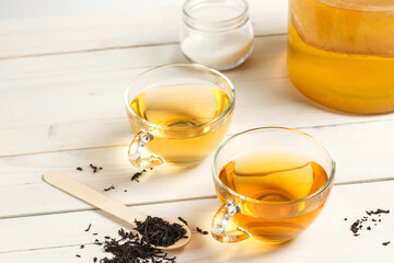 Two glass cups of Kombucha tea, a sweet and sour carbonated drink originally from China. On a light wooden background