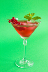 Drink with red currants in the martini glass on the green background