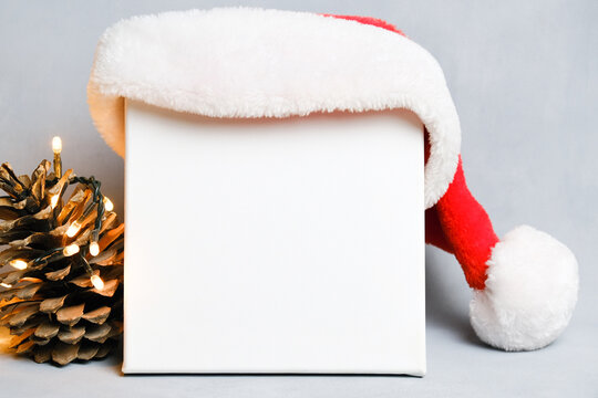 White canvas board for Christmas message. Blank canvas, Santa hat and pine cone with Christmas lights.