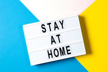 Lightbox with text STAY AT HOME on yellow, pink and light blue background. Top view