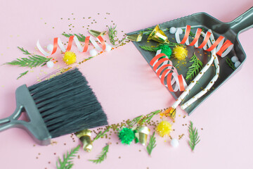 Christmas cleaning after the mess. Cleaning tools broom and scoop and unused Christmas decorations after party top view flat lay on pink background. Concept of cleaning after holiday,