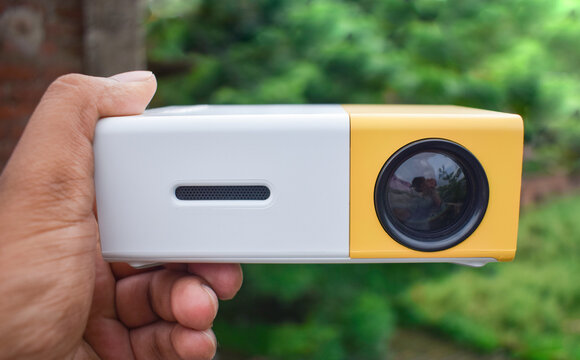 A Mini Projector In Hand With An Outdoor Background, It's A Chinese Low-budget Projector For Kids.