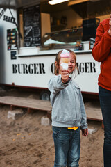 Little girl holding her ice cream in front of her face standing in front of food truck during summer vacations