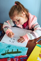Little girl preschooler learning to write letters at home. Kid using crayons doing homework. Concept of early education