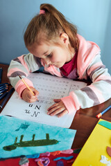 Little girl preschooler learning to write letters at home. Kid using crayons doing homework....