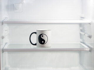 A Ying and Yang cup inside a white lighted refrigerator.