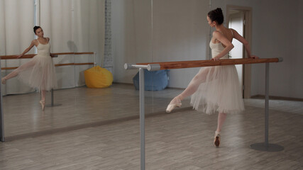 Lovely girl dancer in the ballet hall makes movements with her feet to the side and forward,...