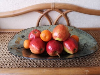 Półmisek owoców, jabłka i mandarynki na ratanowej półce