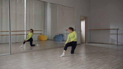 Obraz premium Jump with split of a beautiful girl contemporary dancer. Spacious Studio with a large mirror in the dance school. Training with a warm-up.