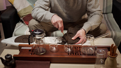 Traditional eastern chinese tea ceremony at home. A man picks pieces from a tile of compressed black tea with a special tea knife. 