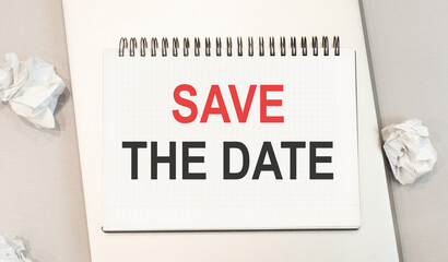 The word save the date is written in a notebook that sits on a gray desktop along with a laptop.