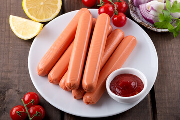 Composition of sausages, ketchup, cherry tomatoes and lemon slices, on white plate. Product of fast preparation